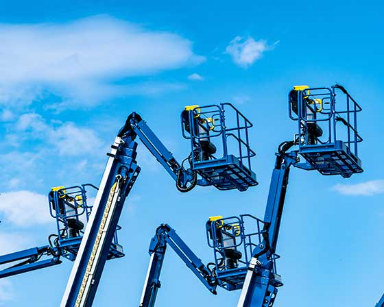several extended boom lifts with the sky in the background